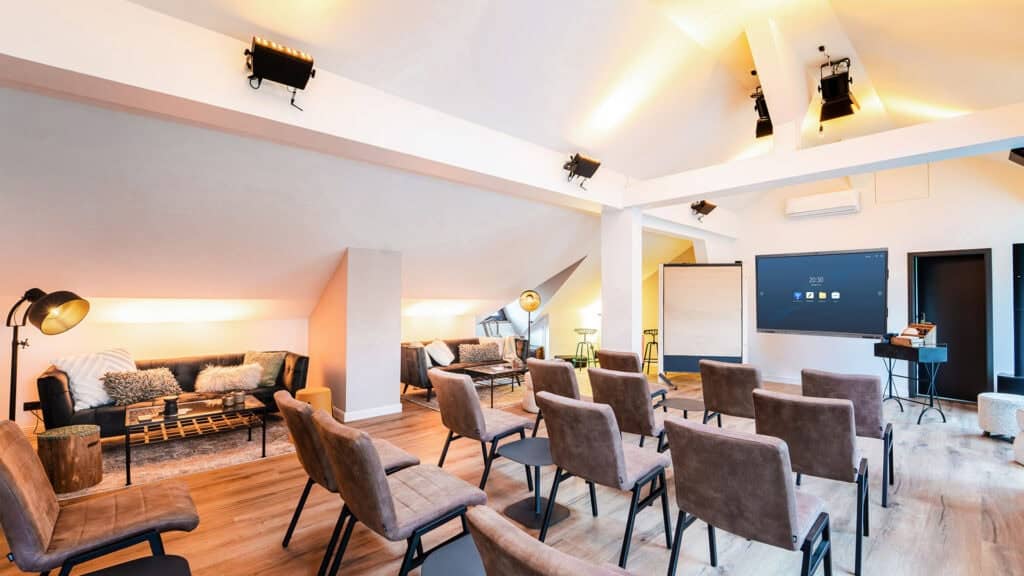 Moderner Besprechungsraum mit Reihen brauner Stühle vor einem großen Bildschirm, sanfter Beleuchtung, Sofas und Arbeitstischen im Hintergrund – ideal für Führungssitzungen oder exklusive Führungskräfteseminare der Generation Gold.