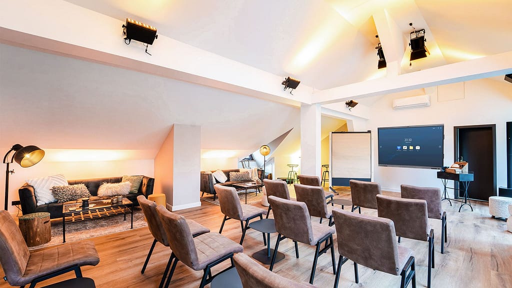 Moderner Besprechungsraum mit Reihen brauner Stühle vor einem großen Bildschirm, sanfter Beleuchtung, Sofas und Arbeitstischen im Hintergrund – ideal für Führungssitzungen oder exklusive Führungskräfteseminare der Generation Gold.