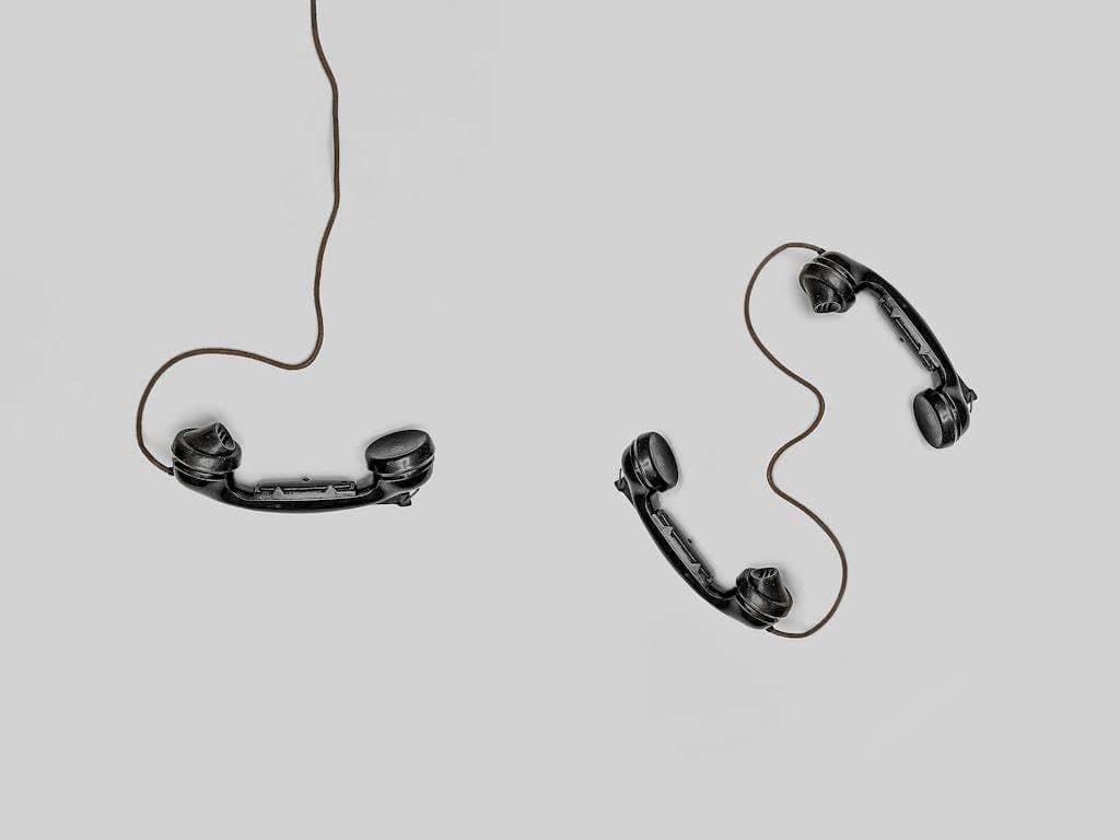 Zwei altmodische schwarze Telefonhörer mit Kabeln liegen auf einer schlichten grauen Oberfläche – ein Hörer steht allein, während der andere mit seinem Gegenstück verbunden ist, was Themen wie Führung und Verbindung zwischen Generationen, wie etwa Generation Gold, aufruft.