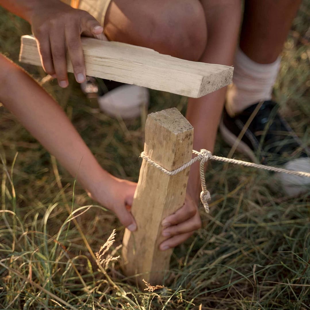 Children working together to hammer a wooden stake during a summer camp activity.
