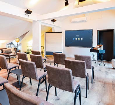 Kleiner Konferenzraum mit braunen Stuhlreihen vor einem großen Wandbildschirm, ideal für Leadership- oder Führungskräfteseminare im Campus 54:2. Moderne Einrichtung, helle Beleuchtung und Lounge-Sitzgelegenheiten schaffen eine inspirierende Atmosphäre.